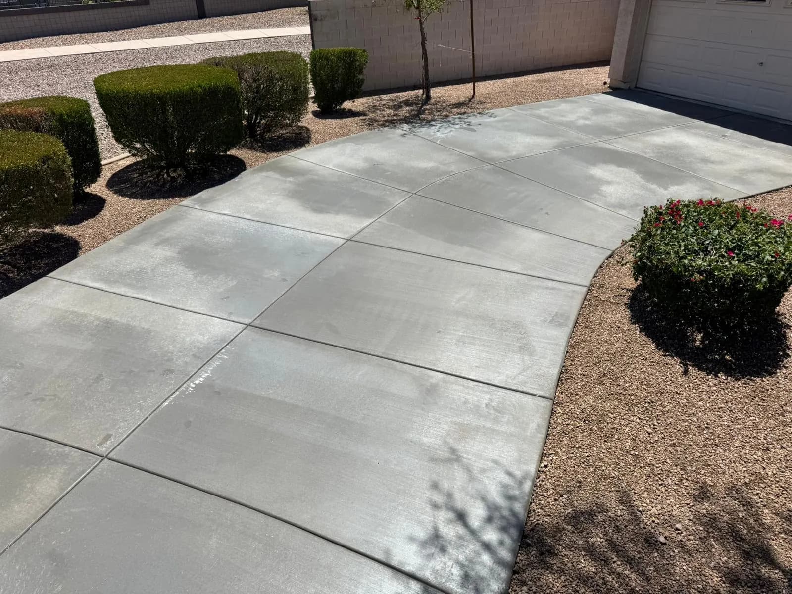 Wide broom-finished concrete driveway with saw-cut control joints, bordered by trimmed hedges and decorative rock