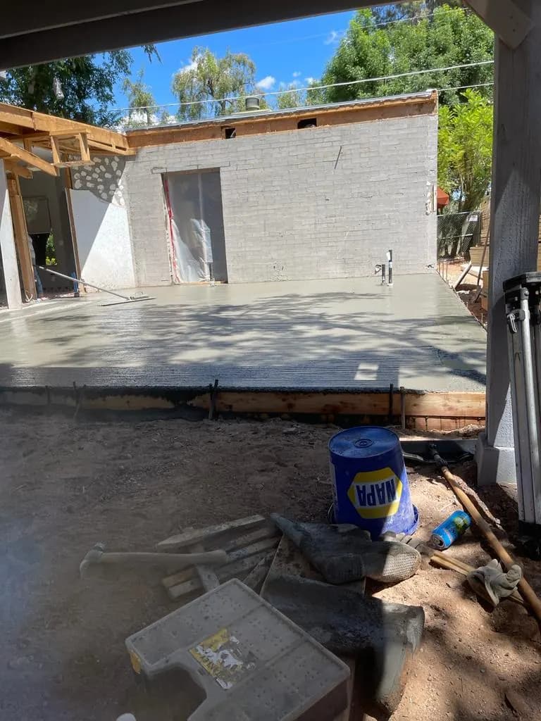 Finished concrete patio slab under a newly framed covered patio structure at a white brick home