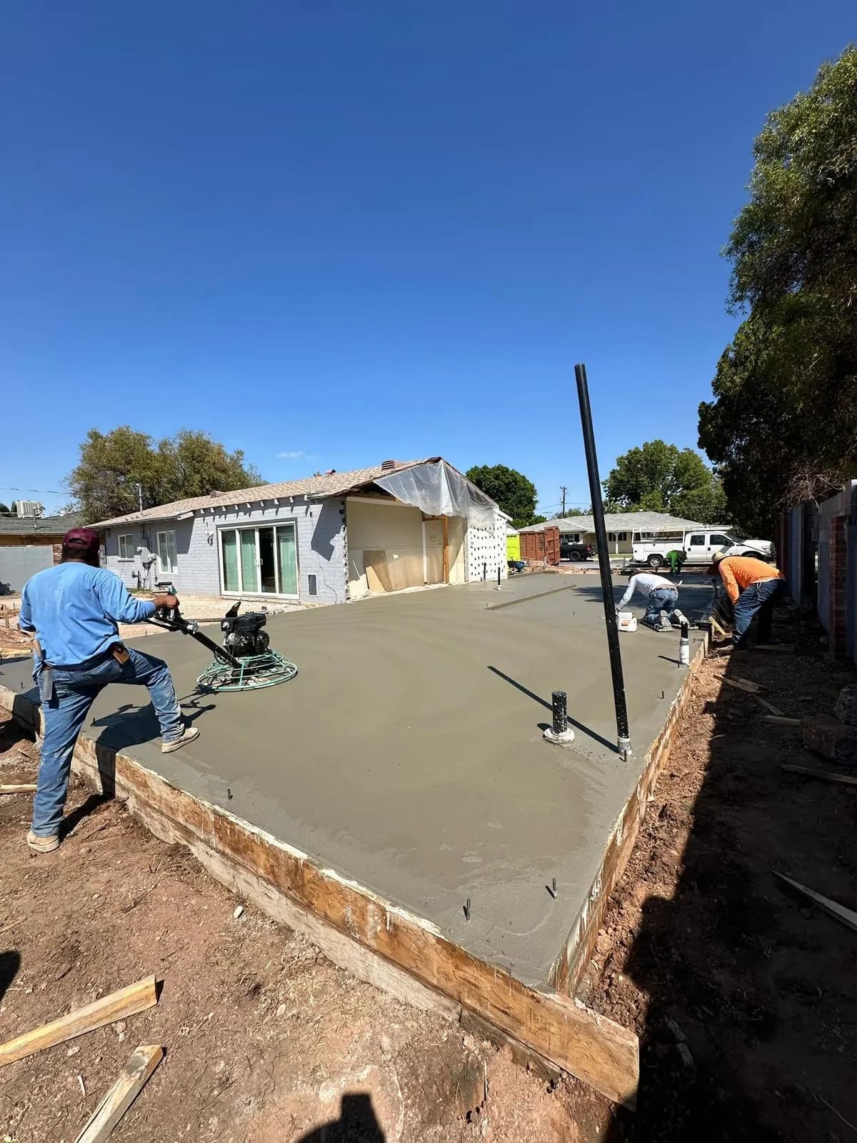 Crew finishing a large freshly poured concrete slab held in wood forms in a backyard