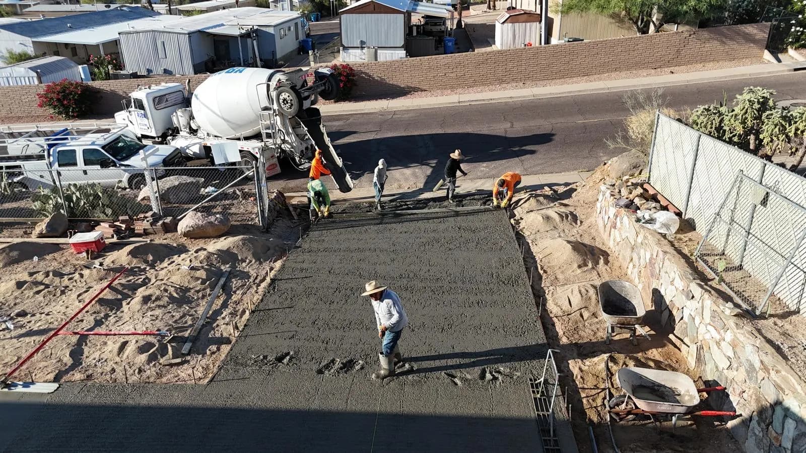 Elevated view of a crew placing and screeding a concrete slab with a mixer truck parked at the street