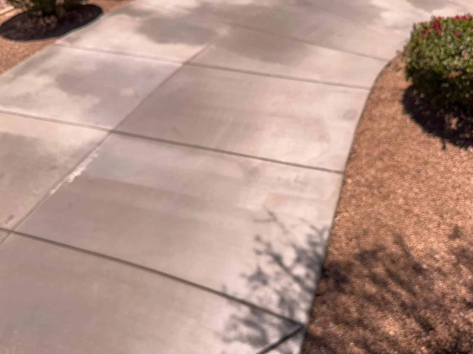 Curved edge of a finished concrete driveway meeting decorative rock landscaping