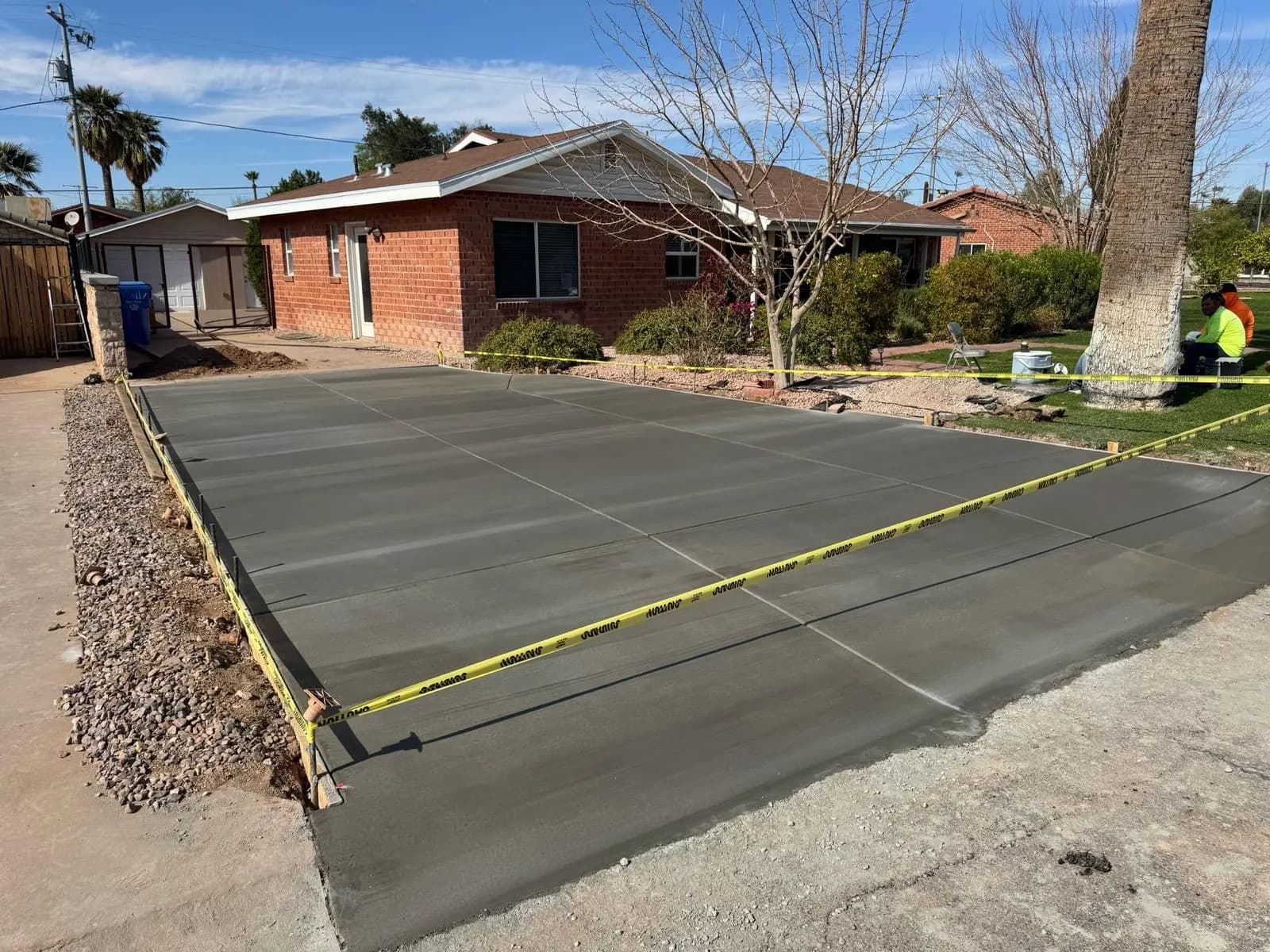 Freshly poured concrete driveway roped off with caution tape in front of a brick ranch-style home