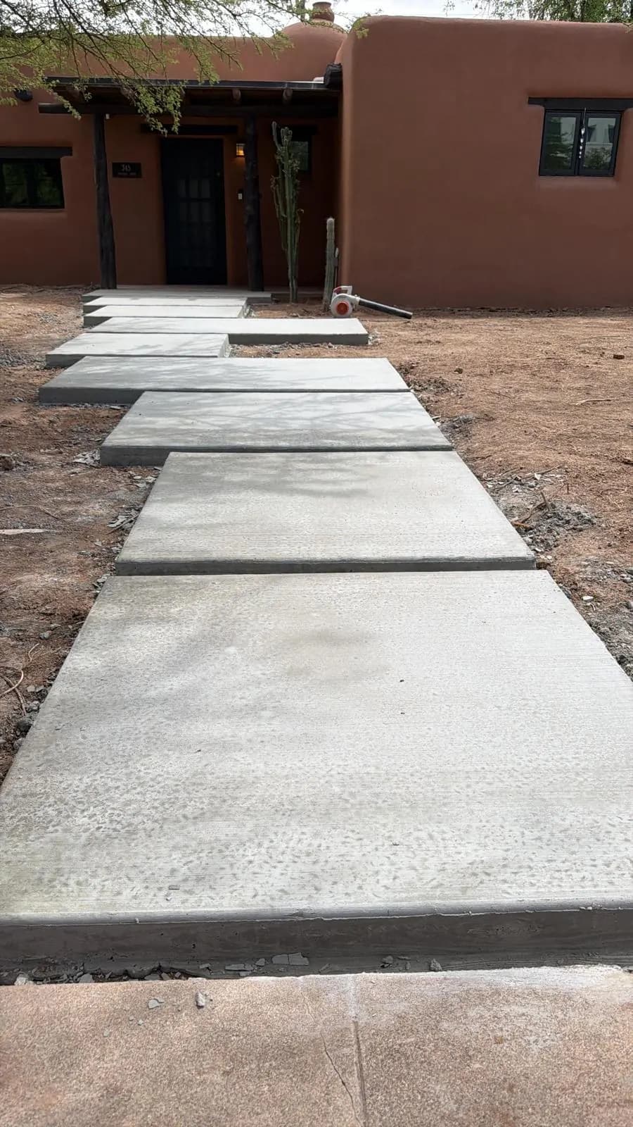 Concrete walkway with stepped landing pads leading to the entry of an adobe-style home