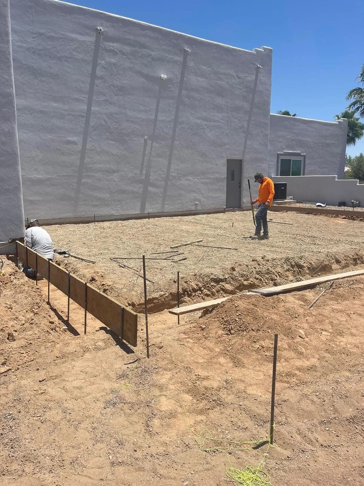 Wood forms and graded subgrade staked out beside a block wall with a crew member raking the base