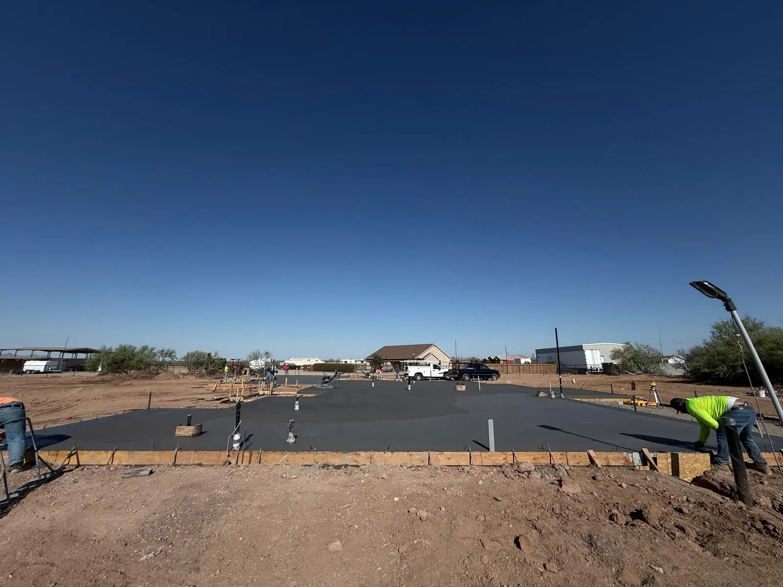 Large fresh concrete foundation slab with crew and edge forms on an open lot at dusk