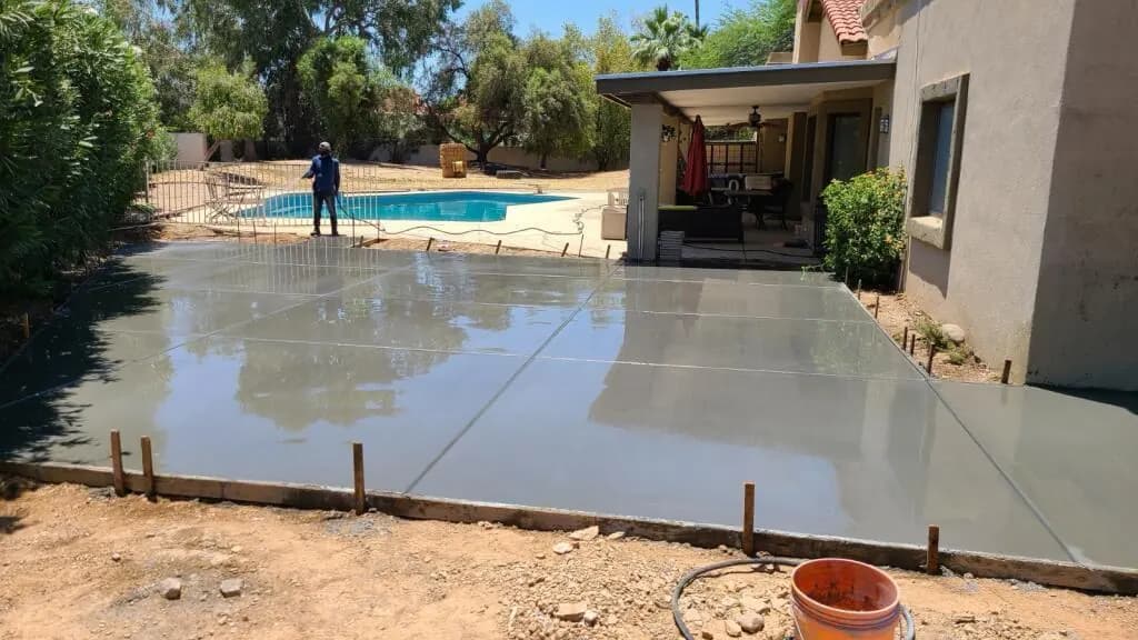 Freshly poured concrete patio slab running alongside a backyard swimming pool