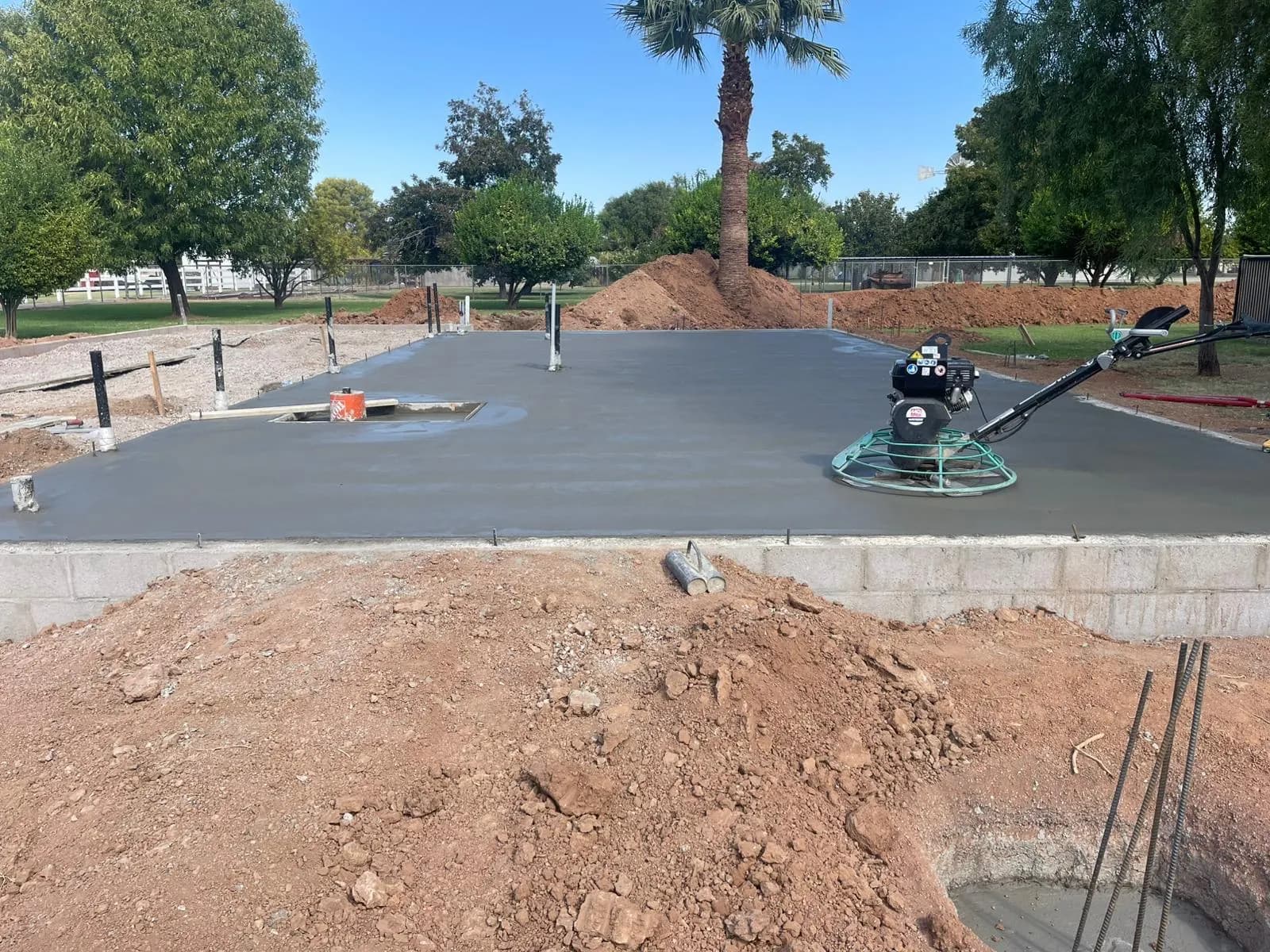 Ride-behind power trowel finishing a large fresh foundation slab framed by a block stem wall