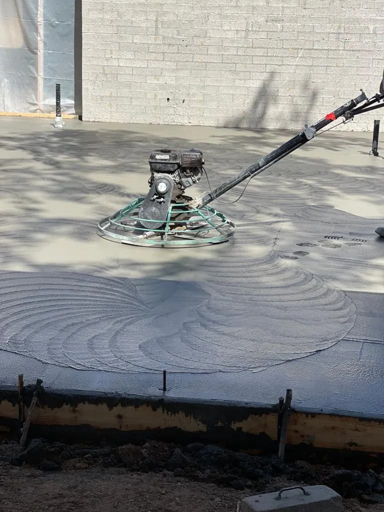 Ride-behind power trowel machine finishing a fresh concrete slab next to a block wall
