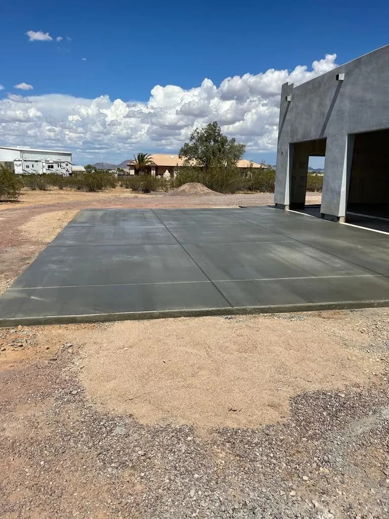 Wide finished concrete pad in front of a tall RV garage building on a desert lot