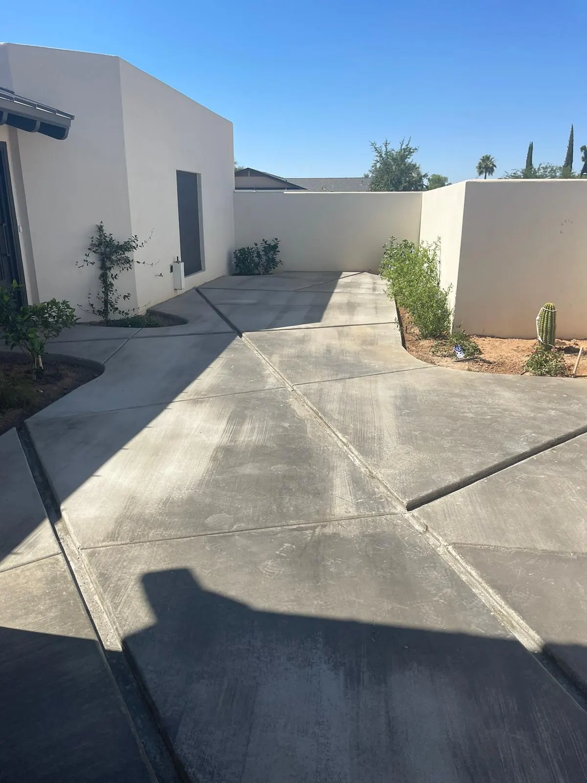 Finished concrete walkway with saw-cut joints running between white stucco walls with desert planting