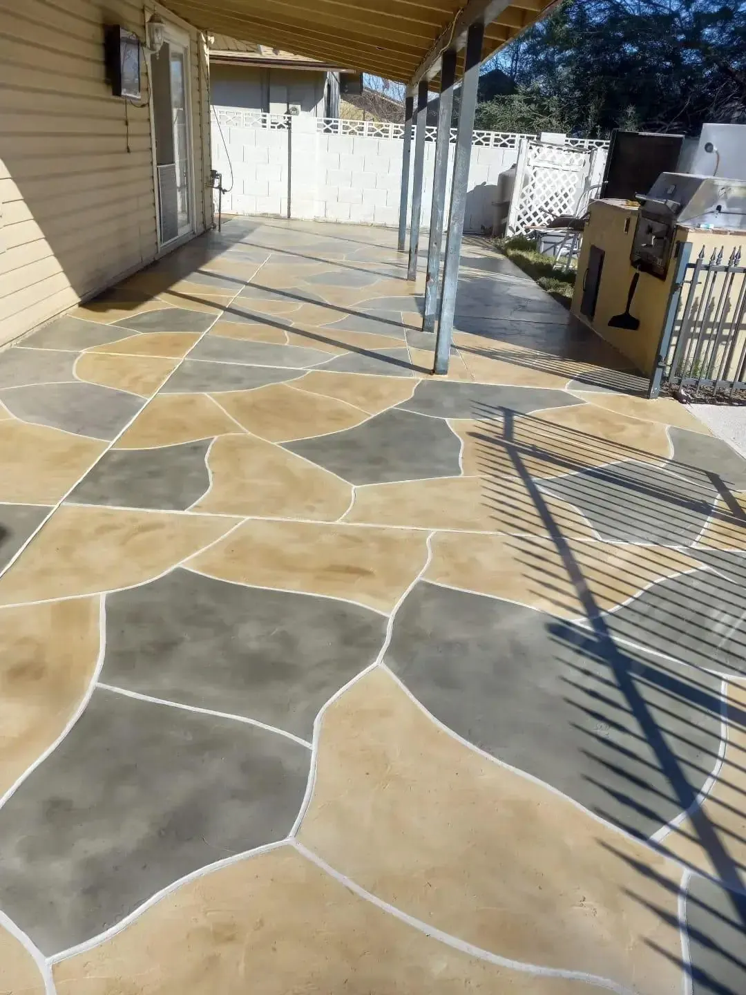 Stained decorative concrete in a hand-cut flagstone pattern, in tan and gray, on a covered backyard patio