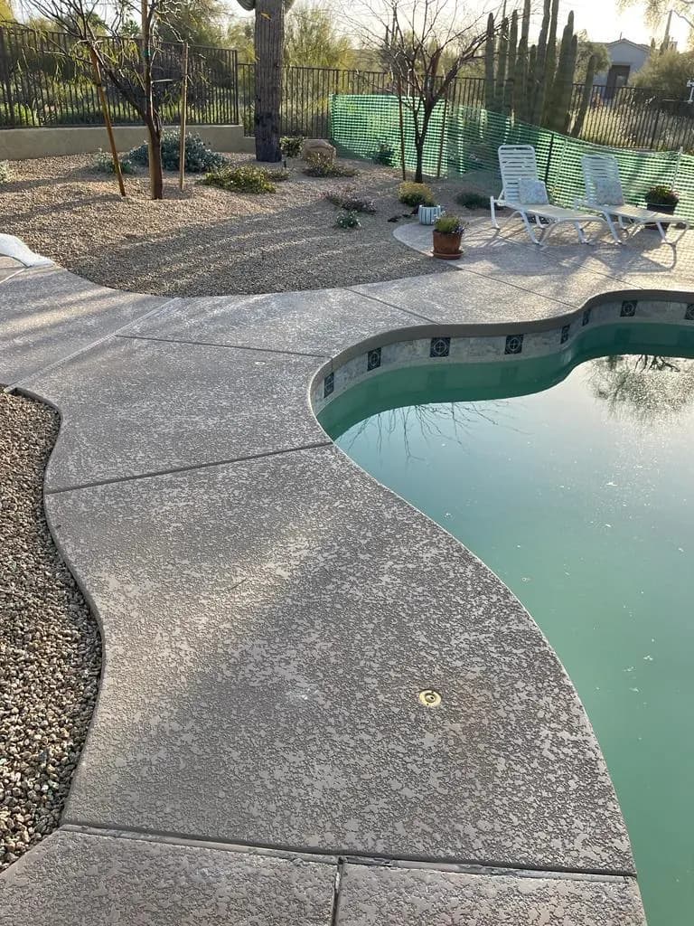 Textured decorative concrete pool deck curving around a backyard swimming pool with desert landscaping behind it